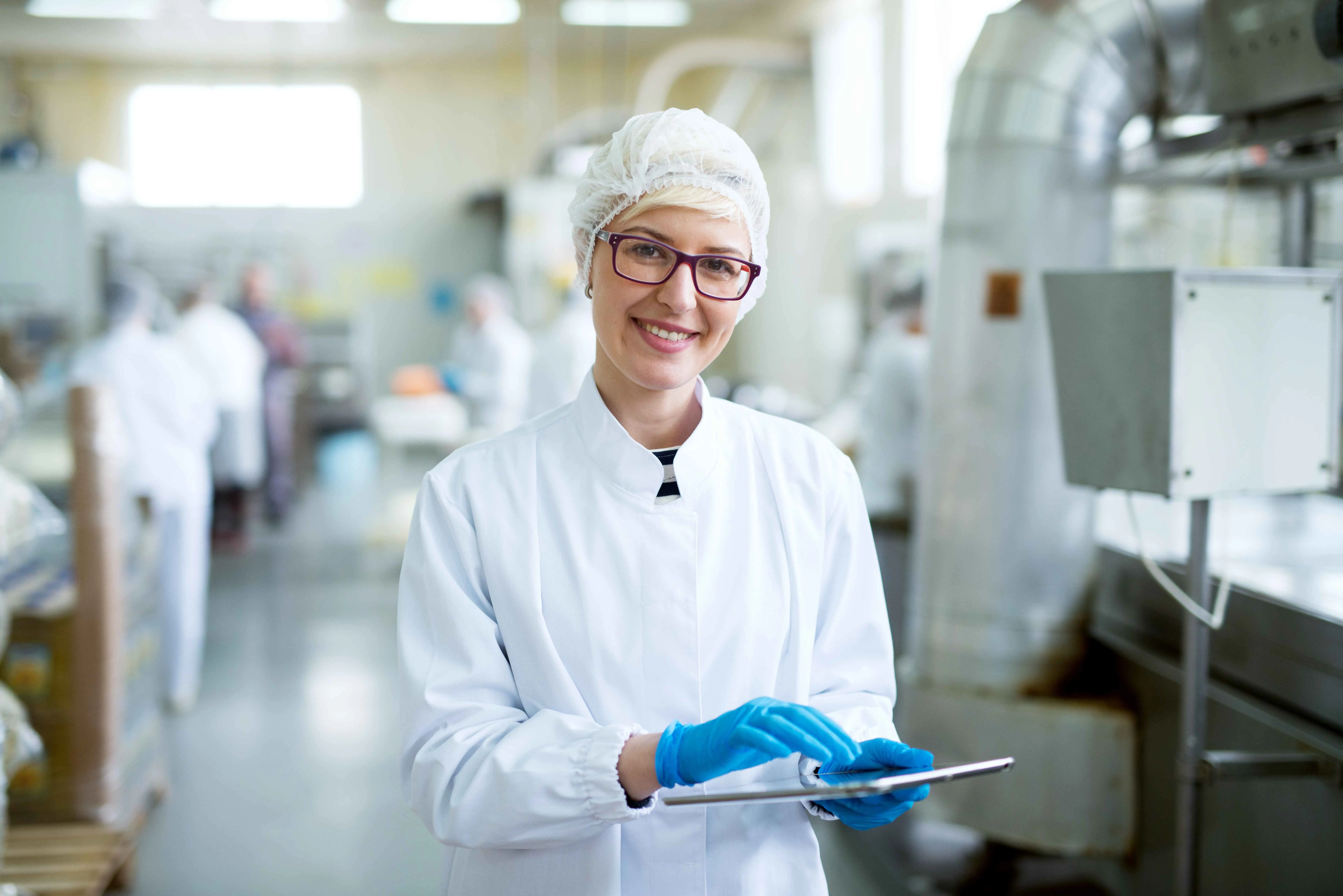 Een productiemedewerker in een witte overal en blauwe handschoenen, een bril en een witmutsje