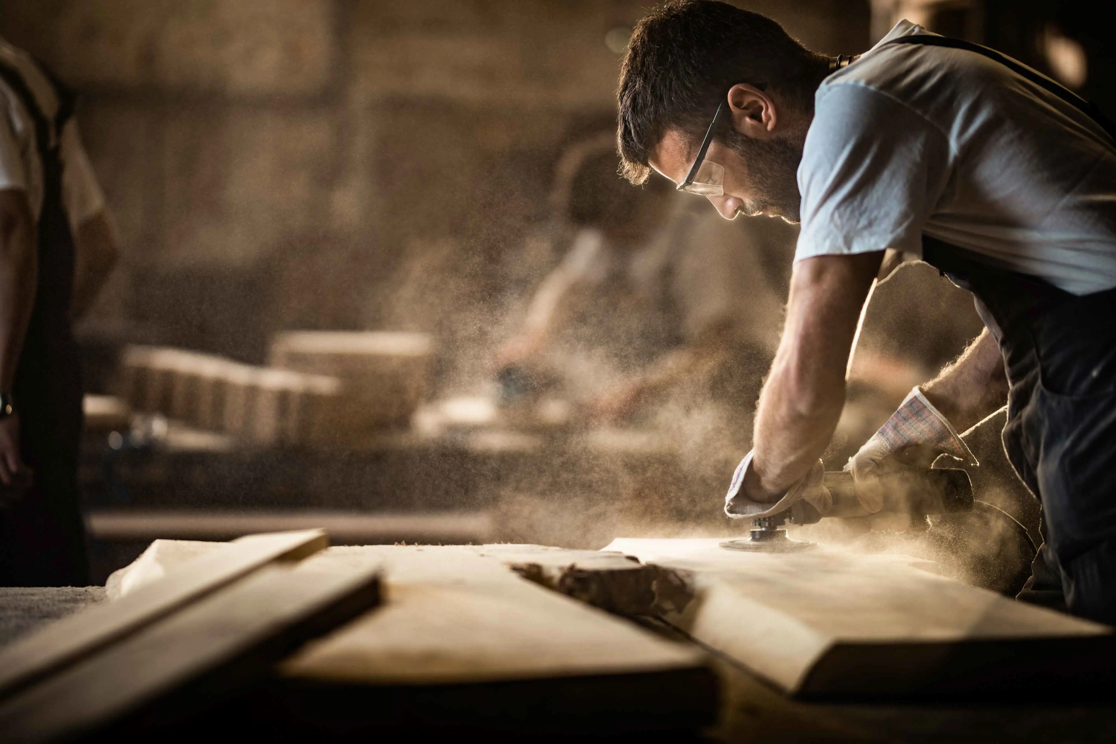 Een man in een overal die hout aan het bewerken is met een schuurmachine