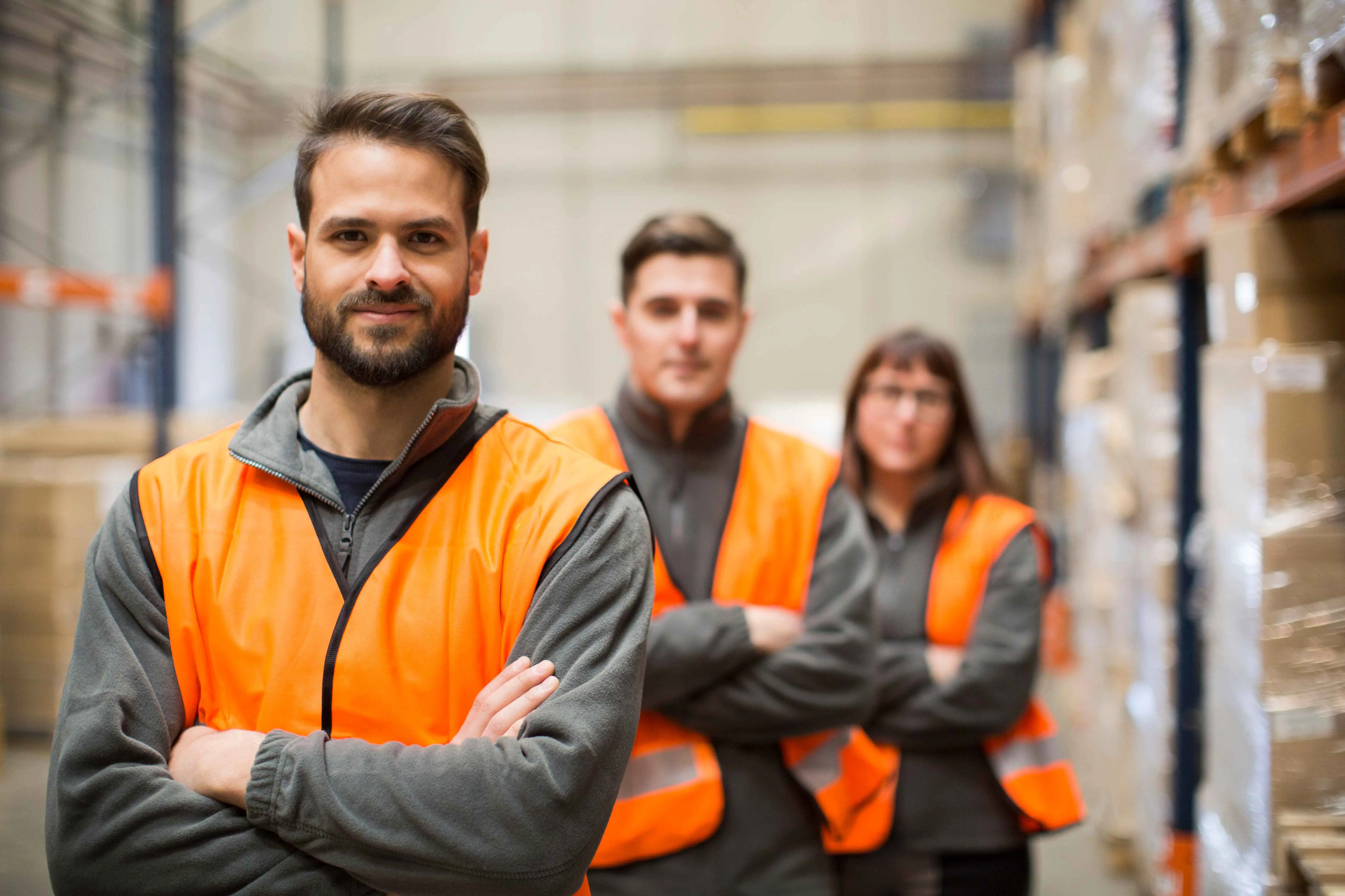 DRIE PERSONEN IN EEN ORANJE FLUOVESTJE ACHTER ELKAAR IN EEN MAGAZIJN